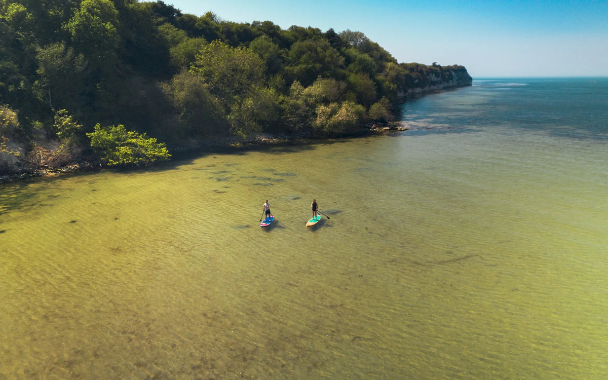 Two people paddleboarding on inflatable paddleboards in clear shallow coastal water